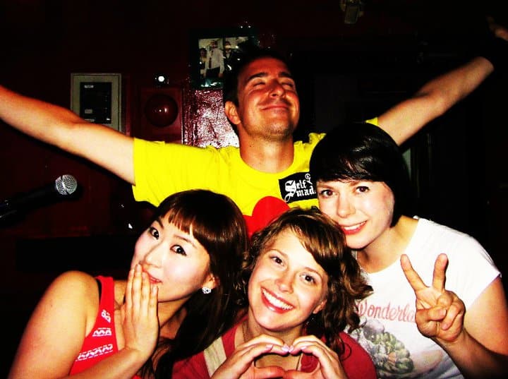 Alice and three friends posing together at a bar, one making peace signs and one a heart with her hands