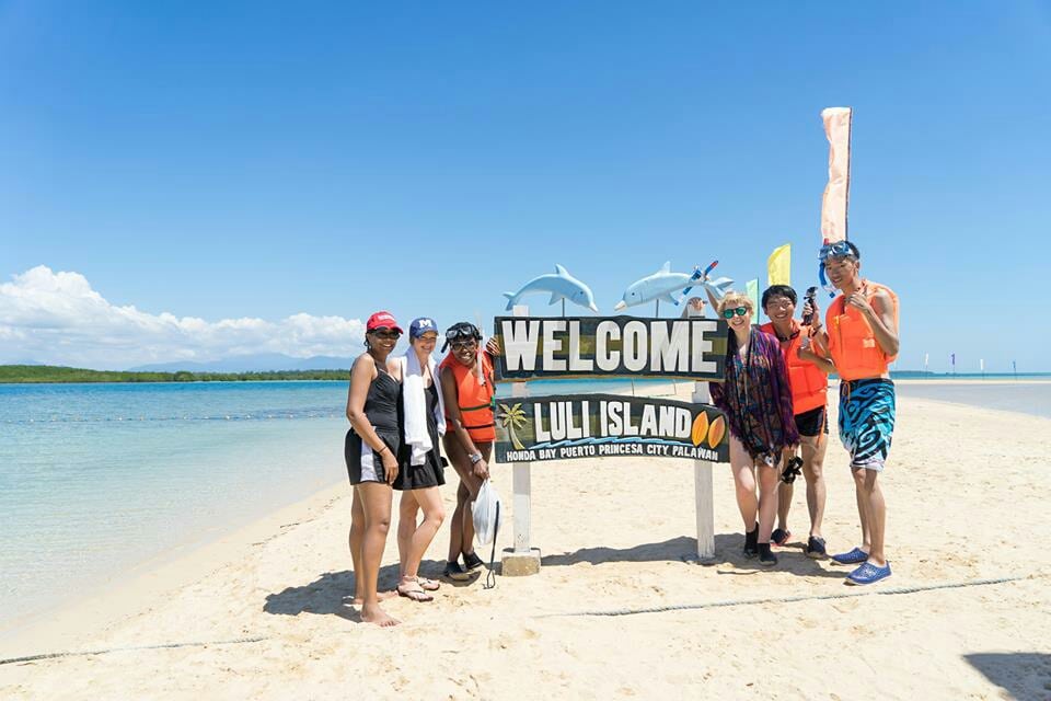 Six travellers pose by the Welcome to Luli Island sign on a white sandbar at Honda Bay, Palawan.