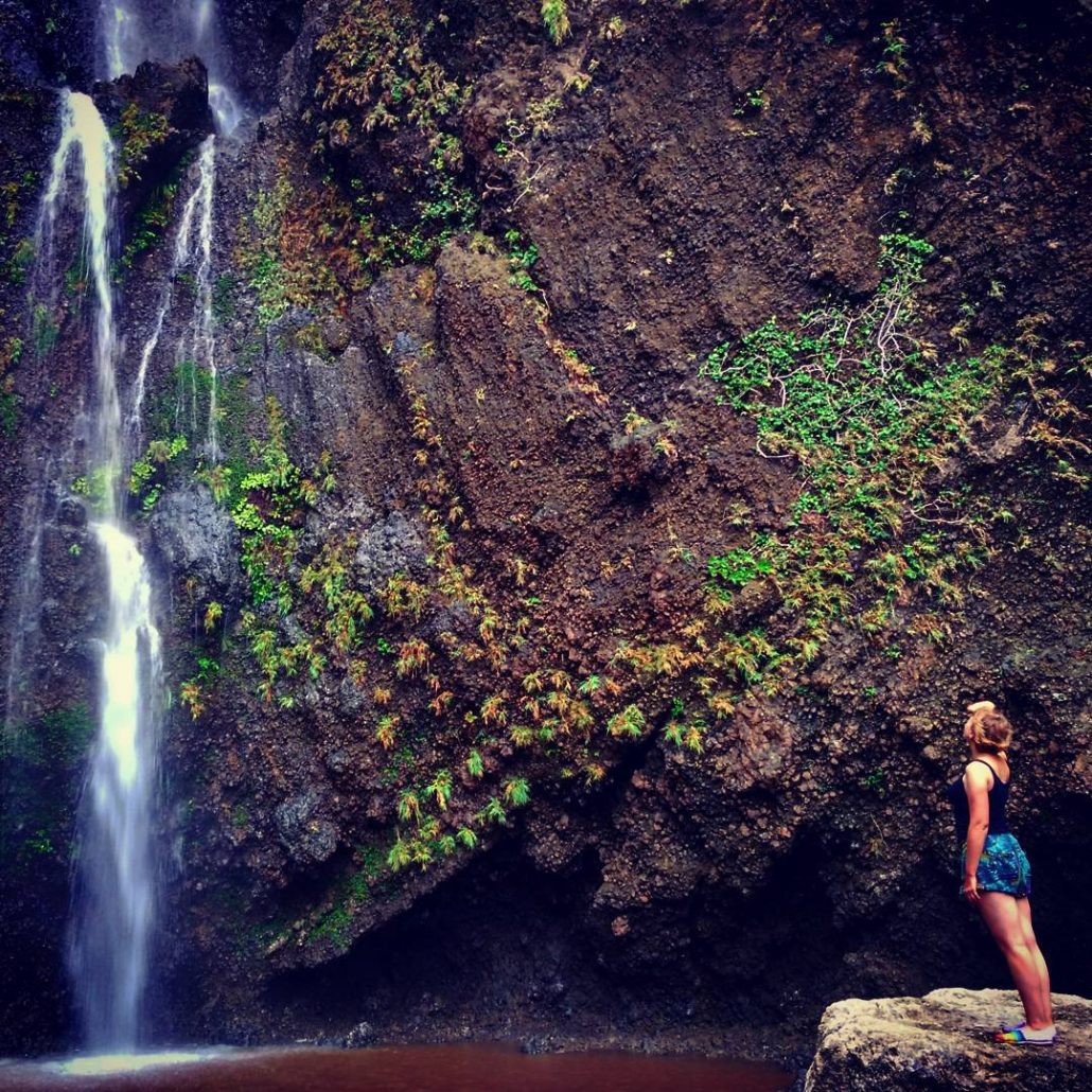 Alice stands on a rock looking up at a tall waterfall over a mossy cliff on Lanyu Island, Taiwan.