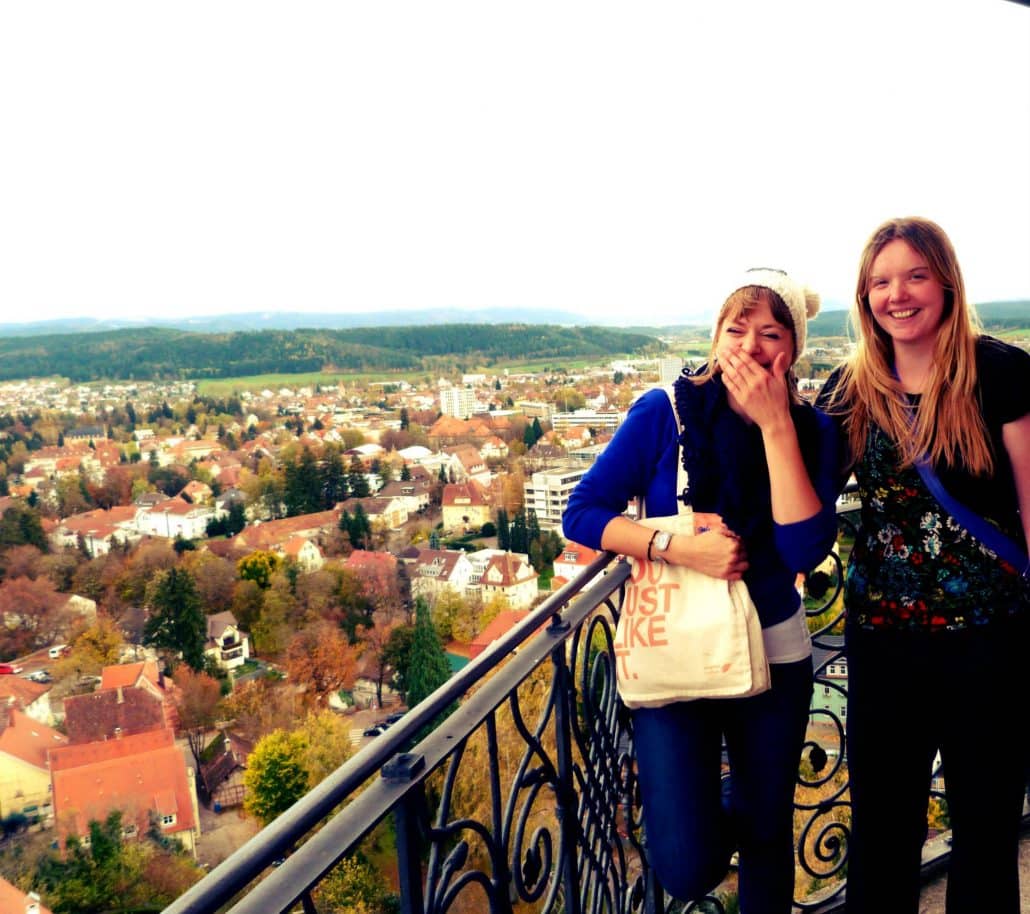 Alice and a friend laughing on a viewing balcony above a German town and rolling wooded hills.