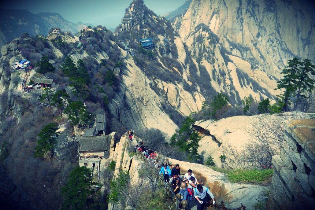 Crowds of visitors on stone stairways winding between the granite peaks of Mount Hua, China.