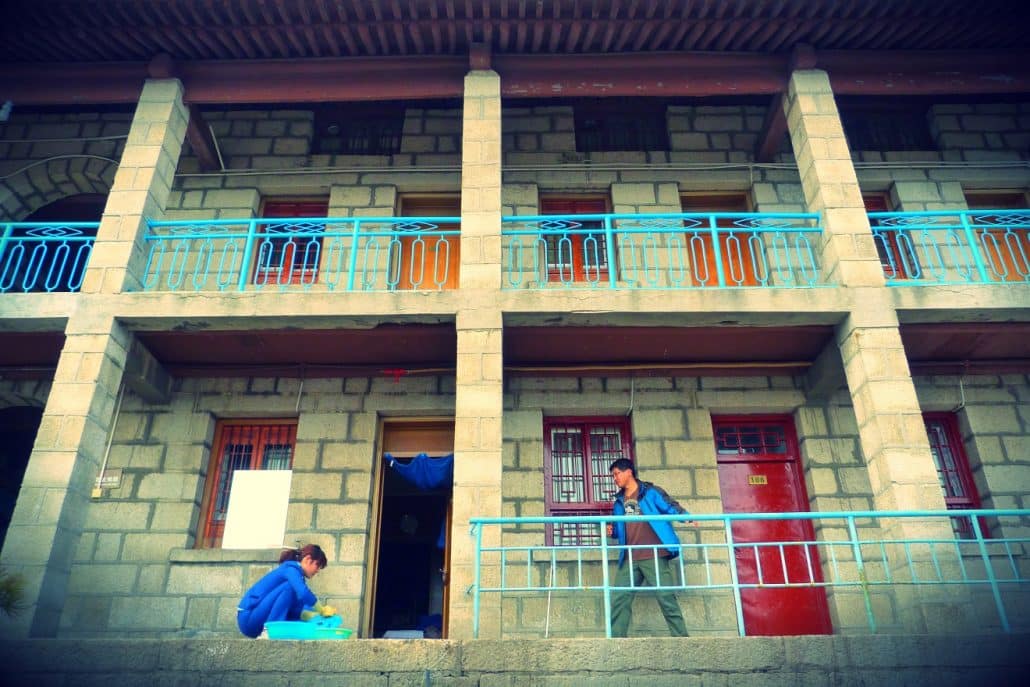 Two people on the balconies of a stone guesthouse with turquoise railings on Mount Hua.