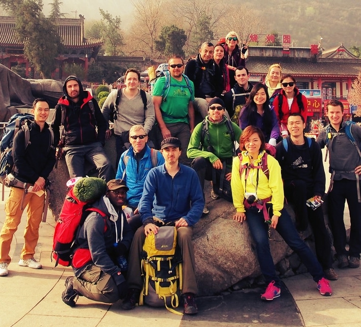 Group of trekkers with backpacks posing by a rock in front of a Chinese temple gate at Mount Hua.