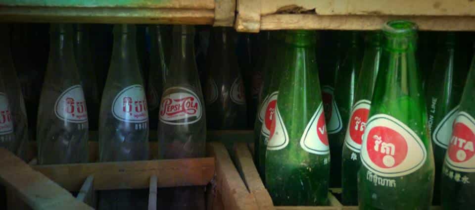 Old glass Pepsi and Vitasoy bottles with Khmer labels stacked in wooden crates in Cambodia.