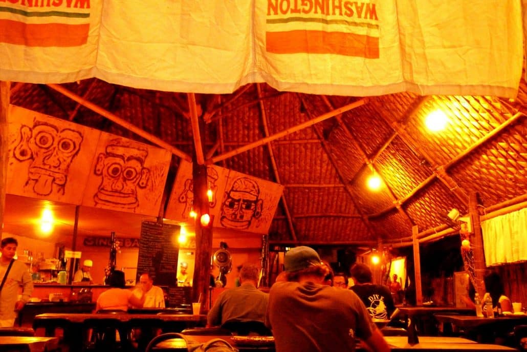 Interior of a thatched-roof restaurant in Coron with hanging banners and diners at wooden tables