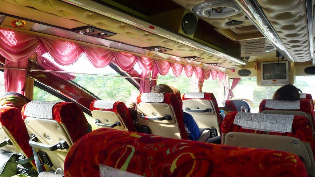 Interior of a long-distance bus with red patterned seats and pink curtains, travelling from Bangkok to Krabi