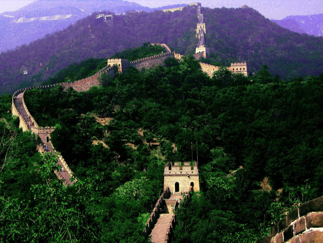 The Great Wall of China winding over green forested hills toward distant mountains