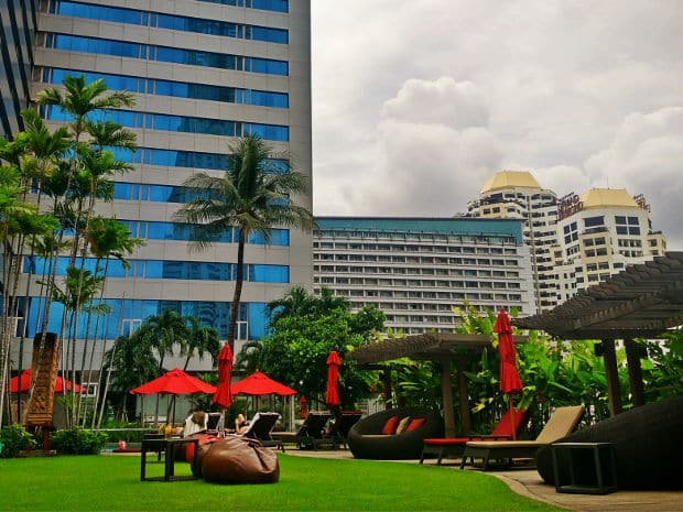 Poolside garden lawn with red umbrellas and loungers, ringed by high-rise buildings at Amari Watergate Bangkok.
