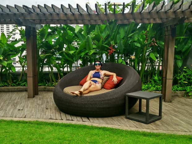 Alice reclines in a bikini on a round wicker daybed under a pergola surrounded by greenery at Amari Watergate Bangkok.