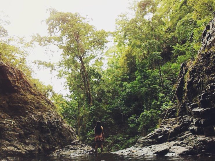 Woman standing in a shallow river between forested rocky cliffs at Bugtong Bato Falls, Philippines