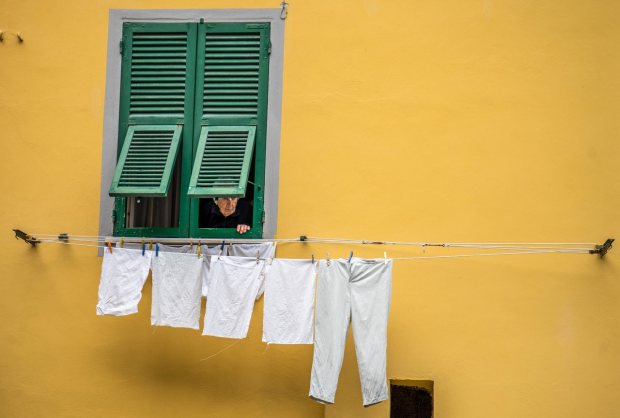 Elderly person looking out a green shuttered window above laundry drying on a line in Italy