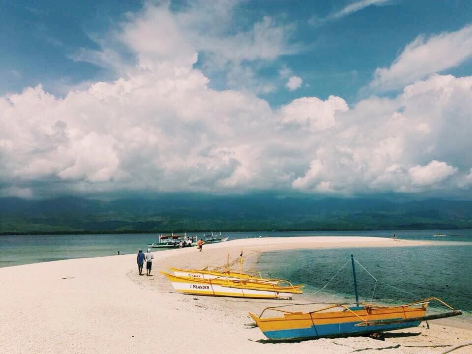 Outrigger boats on a white sandbar at Malalison Island with green hills across the water