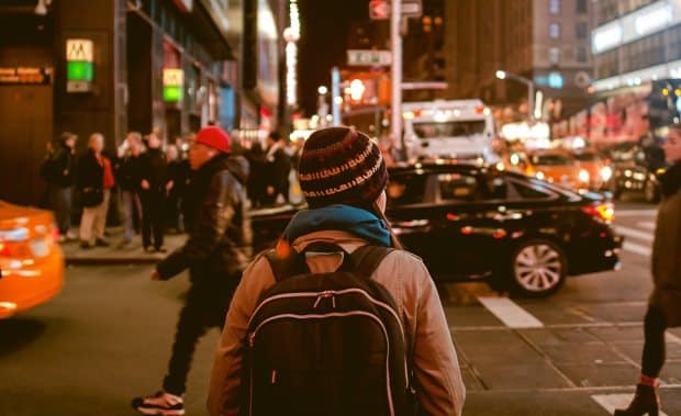 Person in a striped beanie with a backpack waiting at a busy city crosswalk at night
