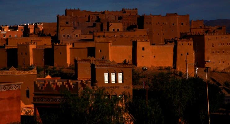 Mud-brick kasbah buildings glowing orange in low evening light in Morocco.