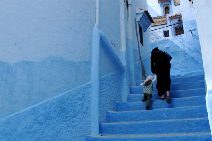 Woman in a robe and small child climbing blue-painted steps in Chefchaouen, Morocco.