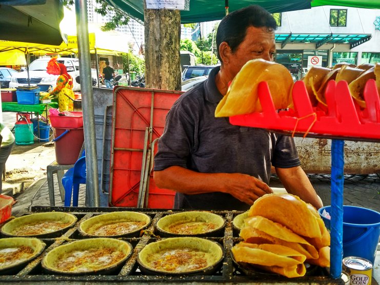 A street vendor in Kuala Lumpur cooking folded apom balik pancakes at a market stall.