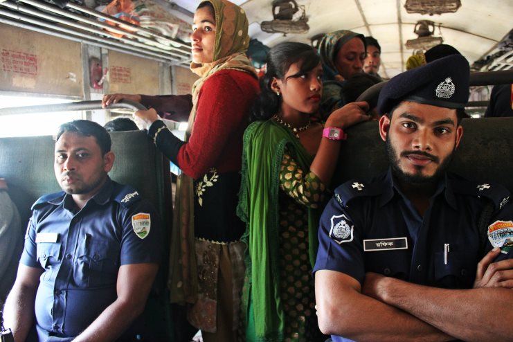 Two uniformed police officers and standing women passengers crowd a train carriage in Bangladesh.