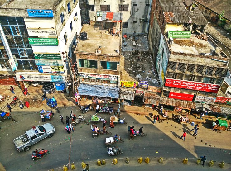 Aerial view of a busy Khulna street corner with rickshaws, shopfronts and Bengali signs.