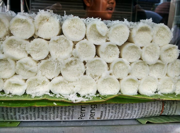 Rows of steamed white putu bambu rice cakes topped with grated coconut on a banana leaf.