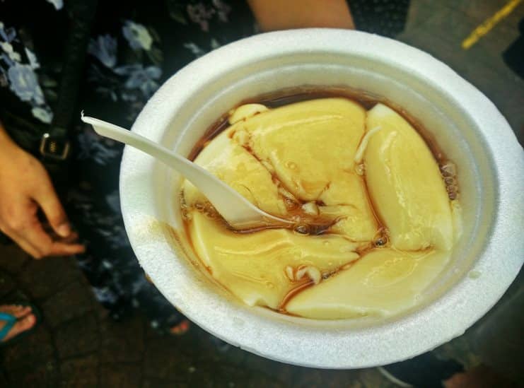 Foam bowl of silky tau foo fah soybean pudding in brown ginger syrup.