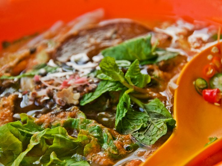 Close-up of asam laksa topped with fresh mint and shredded vegetables in an orange bowl.