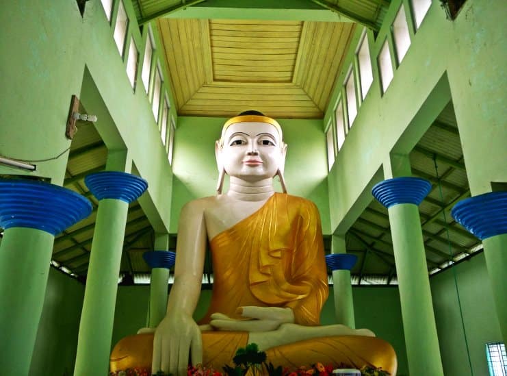 Large golden seated Buddha statue inside a green-walled Buddhist temple in Bangladesh.