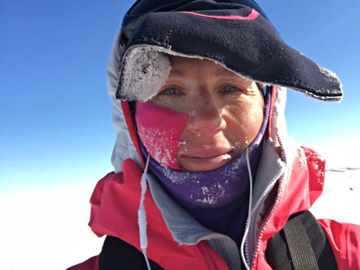 Close-up of a woman's frost-covered face in a pink and black balaclava on a polar ice sheet.