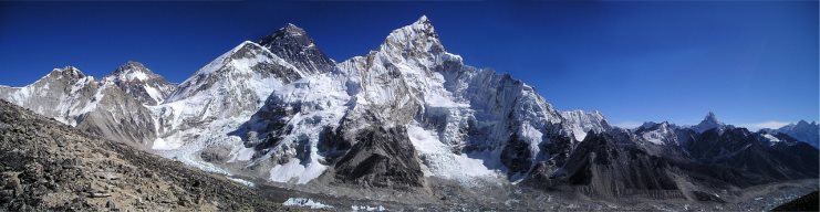 Panorama of Mount Everest and surrounding Himalayan peaks under deep blue sky.