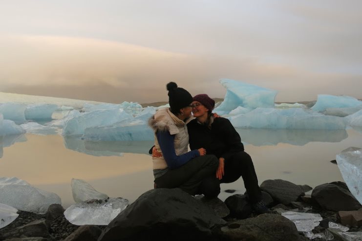 Two women embrace on rocks beside an icy glacier lagoon in Iceland at dusk.