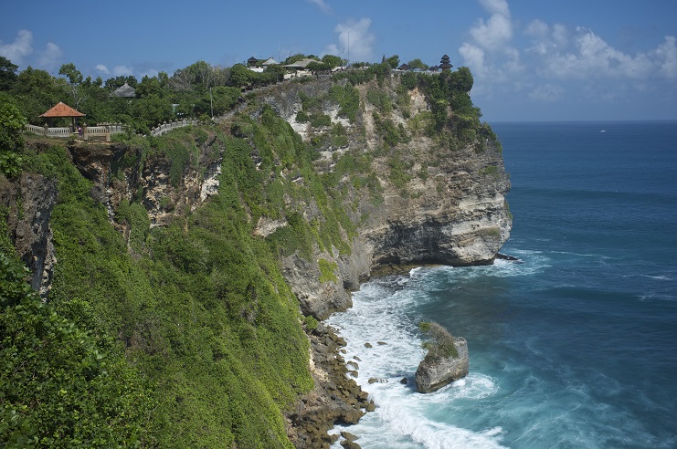 Green clifftop with the Uluwatu temple grounds above sea cliffs meeting the ocean in Bali.