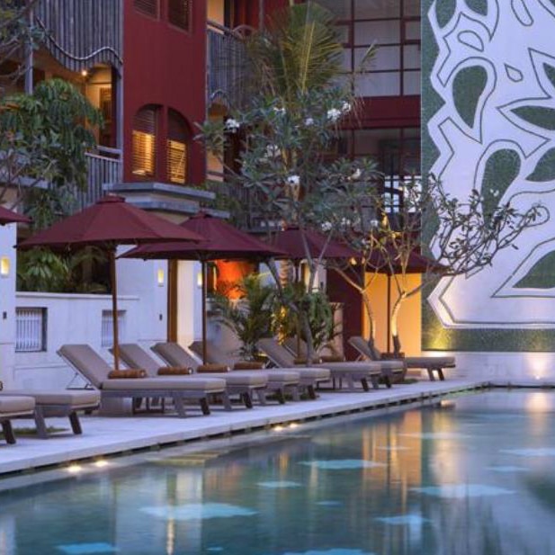 Row of sun loungers under red umbrellas beside a lit pool at Alaya Resort in Bali at dusk.