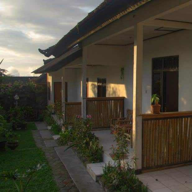Bali guesthouse rooms with bamboo railings and a garden path at sunset.