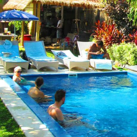 Guests relaxing in and around a garden pool with sun loungers at Cafe Locca Hostel, Bali.