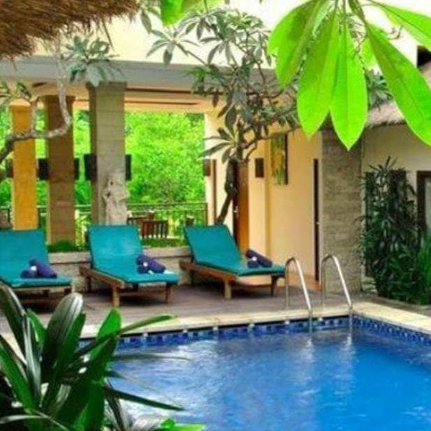 Teal sun loungers on a deck beside a blue pool surrounded by tropical plants at a Bali hotel.