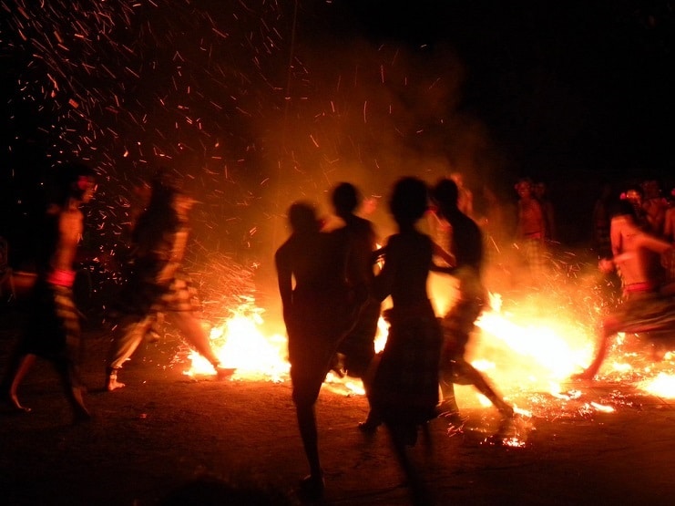Silhouetted dancers moving through flames and flying sparks at a night fire dance in Bali.