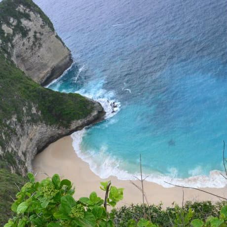 Sandy cove ringed by cliffs and turquoise water below the Full Moon Bungalows viewpoint, Nusa Penida, Bali.
