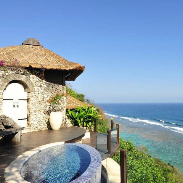 Clifftop villa with a thatched roof, plunge pool and glass railing above the Bali coast.