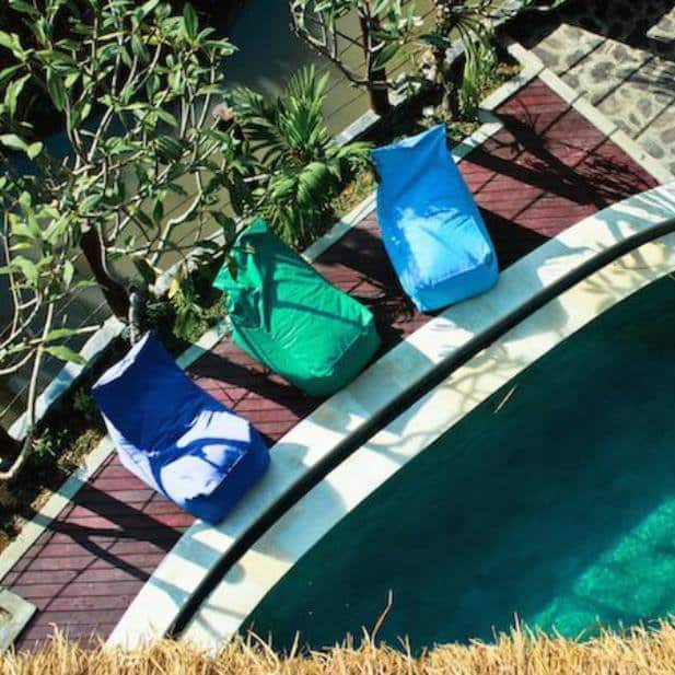 Blue and green beanbag loungers on a wooden deck beside the pool at a Bali surf camp.