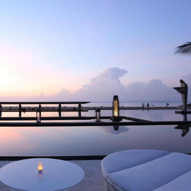 Infinity pool facing the sea at sunset with white daybeds at Mulia Resort, Bali.