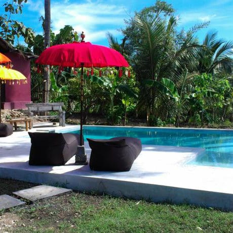 Red Balinese parasol and beanbag loungers beside a pool surrounded by banana trees at Namaste Bungalows, Bali.