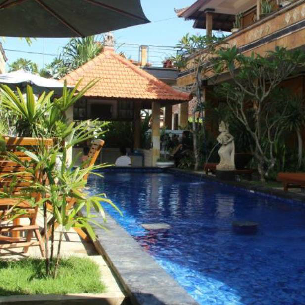 Blue swimming pool with a thatched gazebo and stone statue at Nitya Homestay in Bali.