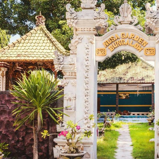 Carved white entrance gate reading Nusa Garden Bungalow beside a small pool and garden in Bali.