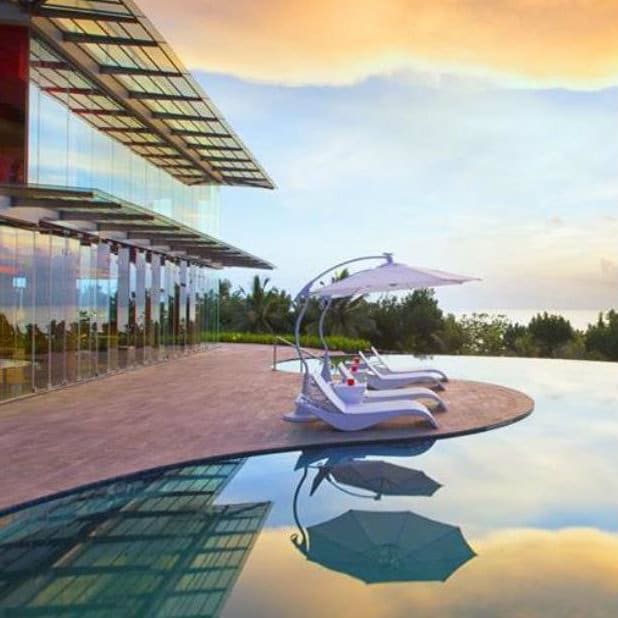 Loungers and a white canopy beside an infinity pool reflecting the sunset at Sheraton Bali Kuta.