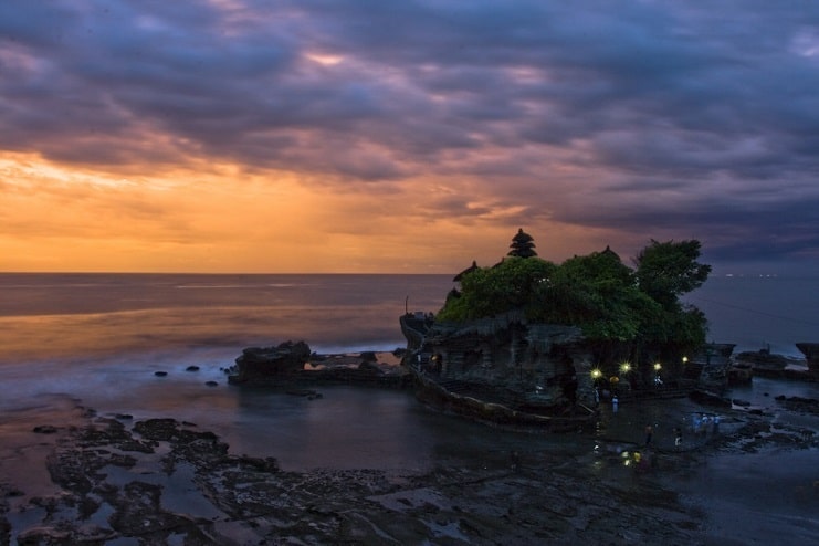 Tanah Lot temple on its rocky outcrop at sunset, with an orange sky over the sea in Bali.