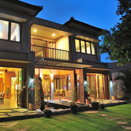 Two-storey villa glowing with warm interior lights at dusk beside a lawn at Villa Sundamala, Bali.