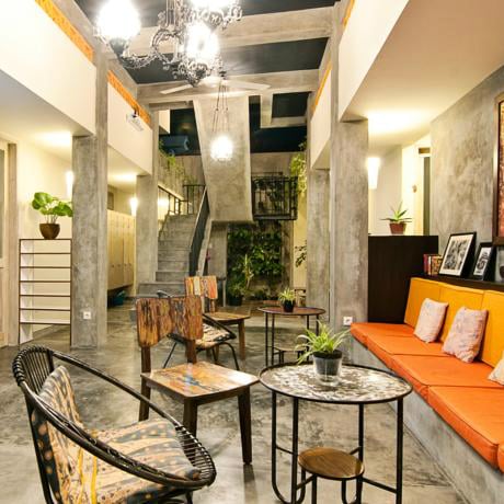 Concrete-walled hostel lounge with an orange bench, mismatched chairs and a chandelier at Bread and Jam in Bali.