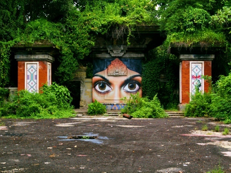 Overgrown abandoned building with a large mural of a woman's eyes and face in Bali.