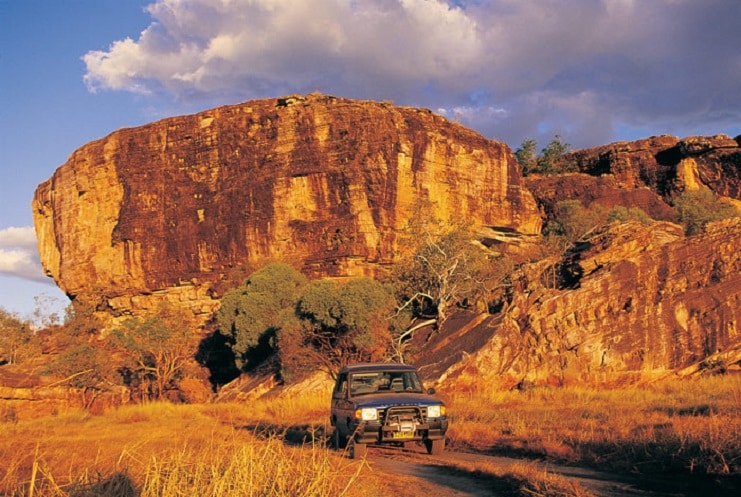 A four-wheel drive on a dirt track beneath red sandstone escarpments in Australia's Northern Territory.
