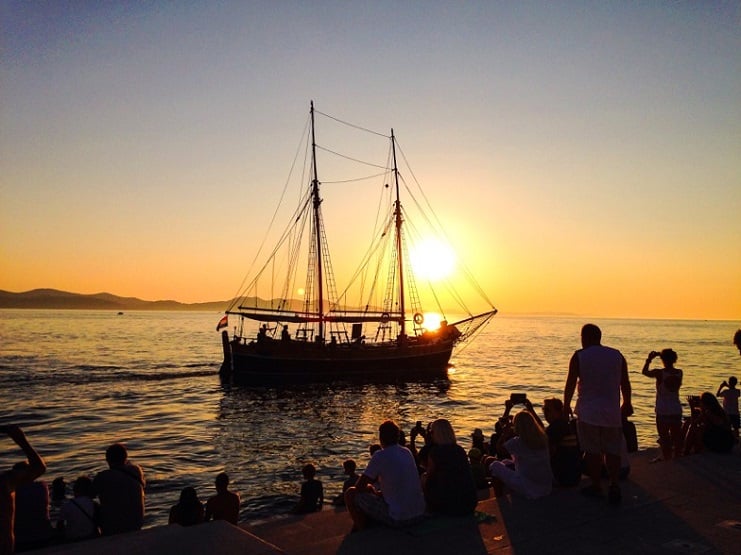 A tall ship silhouetted against the sunset as people watch from the waterfront in Zadar, Croatia.