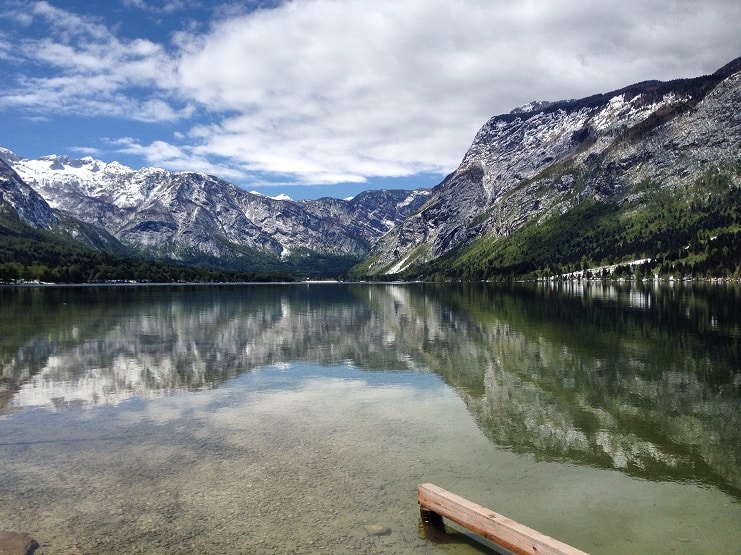Snow-capped mountains reflected in the clear green water of Lake Bohinj, Slovenia.